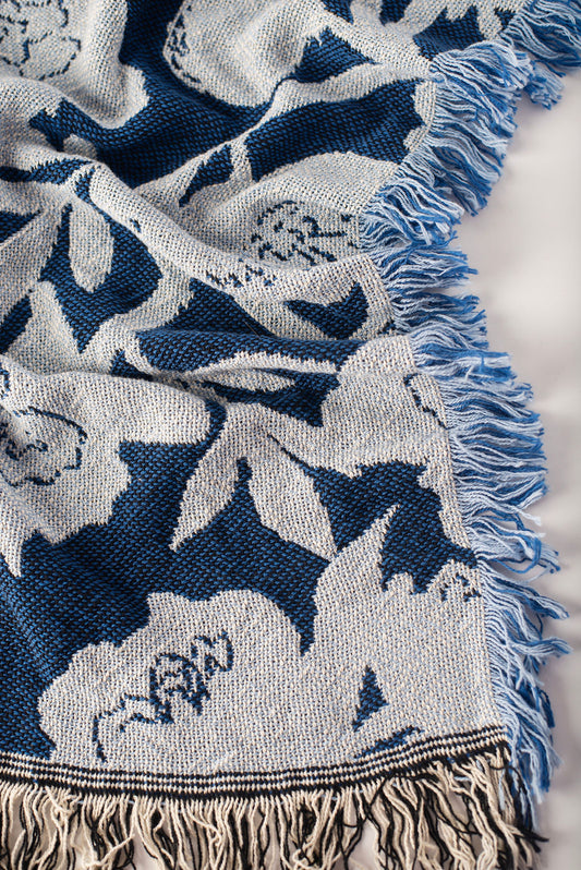 Close-up corner view ow blue and light blue patterned blanket with fringe on a light background