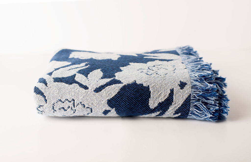 Folded blue and light blue floral blanket from the front side with fringe on a light background