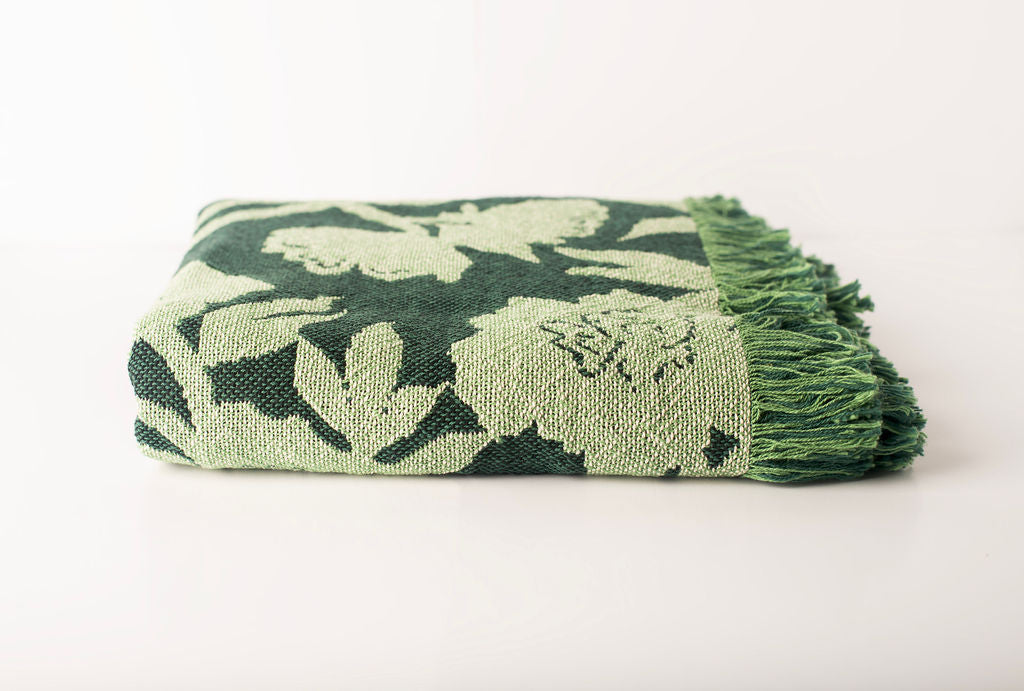 Front view of folded dark green and light green floral woven cotton throw on a white background