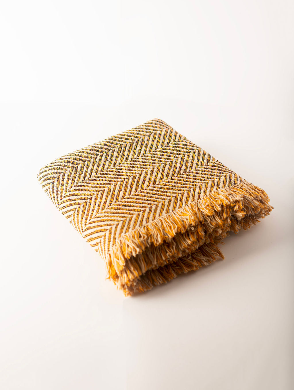 Folded mustard yellow and neutral herringbone blanket on a light background
