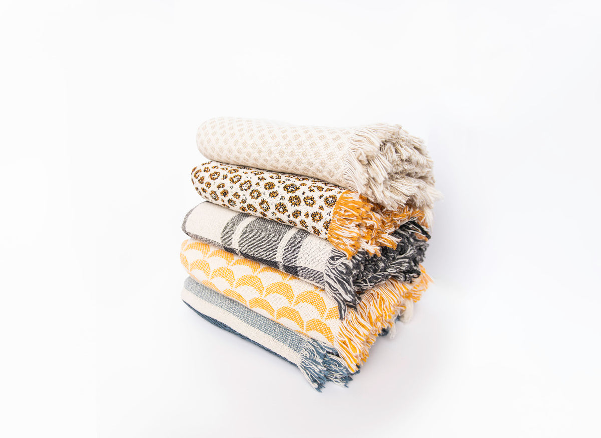 Stack of five Kindly Woven patterned blankets with Sutton Delft coastal stripe at the bottom, angled view