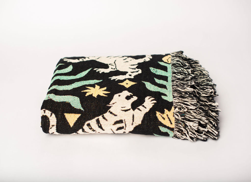 Front view of folded green, black, cream, and gold tiger woven cotton throw on a white background