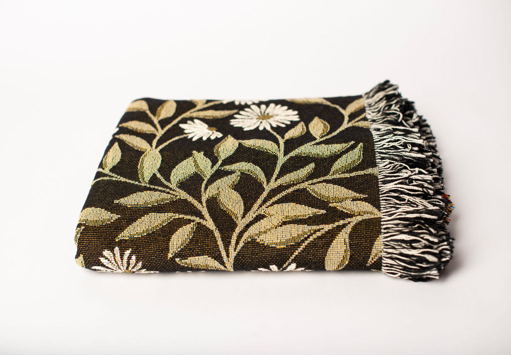 Front view of folded black and gold botanical woven throw blanket with fringe