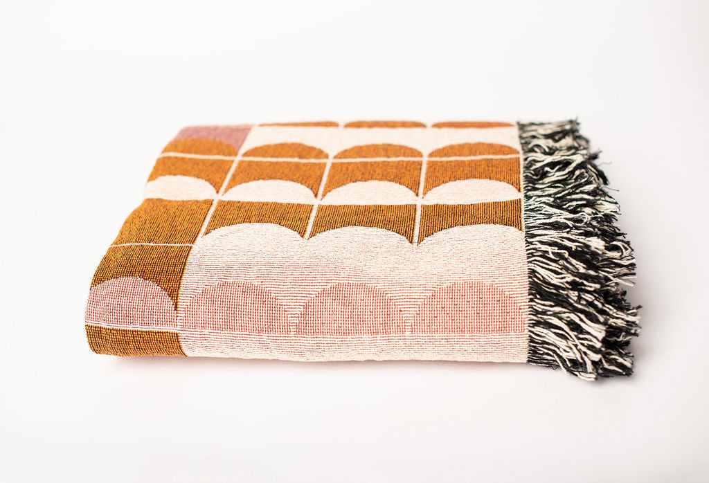 Front view of folded pink, cream, and ochre geometric woven cotton throw on a white background