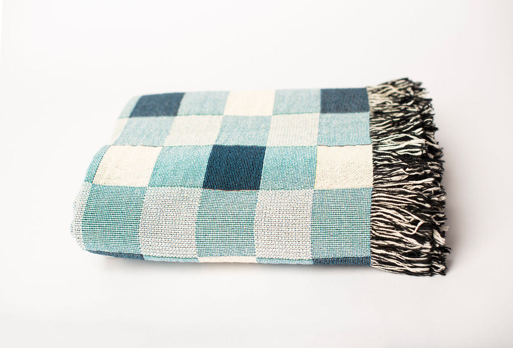 Front view of folded blue, aqua, and cream check woven throw blanket on a white background