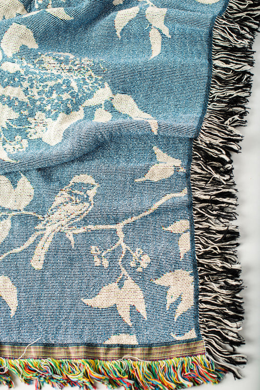 Close-up of Wren Chambray blue and cream bird and botanical woven cotton throw with fringe