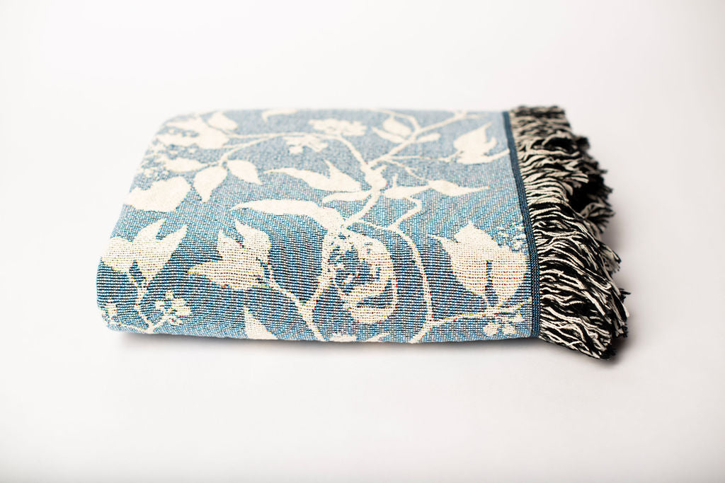 Front view of folded blue and cream bird and botanical woven cotton throw on a white background