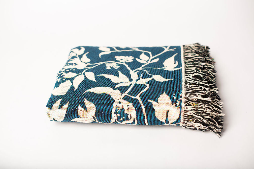 Folded teal and cream bird-patterned woven cotton throw blanket with fringe